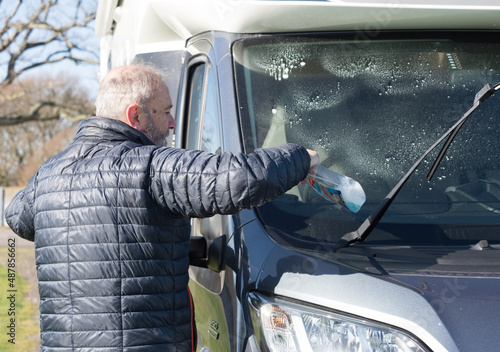 Slika na platnu A bearded male motorhome owner cleans his recreational vehicle front windscreen window