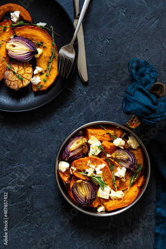 Pan with roasted pumpkin,onion,garlic,thyme and rosemary on dark blue background. Rustic food photography.  Low key.Top view with copy space.