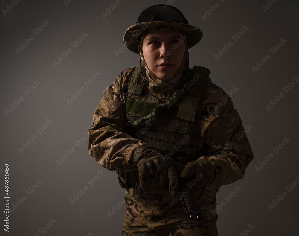 Portrait of  soldier in military camouflage uniform protected with helmet, body armor, Holding machine gun desaturated on a gray background. Military Conflict Actions. Man In camouflage.