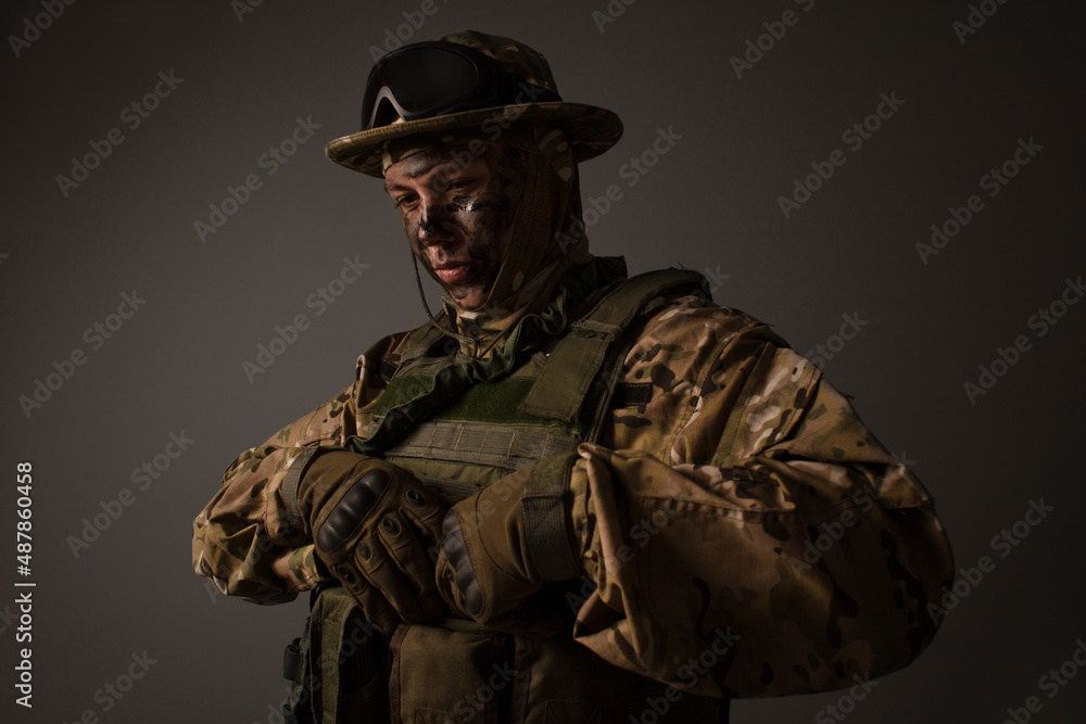 A close-up shot of a military man in a uniform in a hat with goggles giving orders on the grey background. Portrait of the soldier . Calm warrior. Army.  Commando. Call of duty.