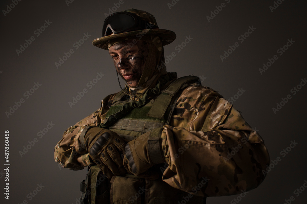 A close-up shot of a military man in a uniform in a hat with goggles giving orders on the grey background. Portrait of the soldier . Calm warrior. Army. Commando. Call of duty. A close-up shot of a military man in a uniform in a hat with goggles giving orders on the grey background. Portrait of the soldier . Calm warrior. Army. Commando. Call of duty.