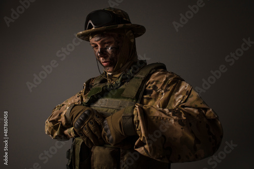 A close-up shot of a military man in a uniform in a hat with goggles giving orders on the grey background. Portrait of the soldier . Calm warrior. Army. Commando. Call of duty.