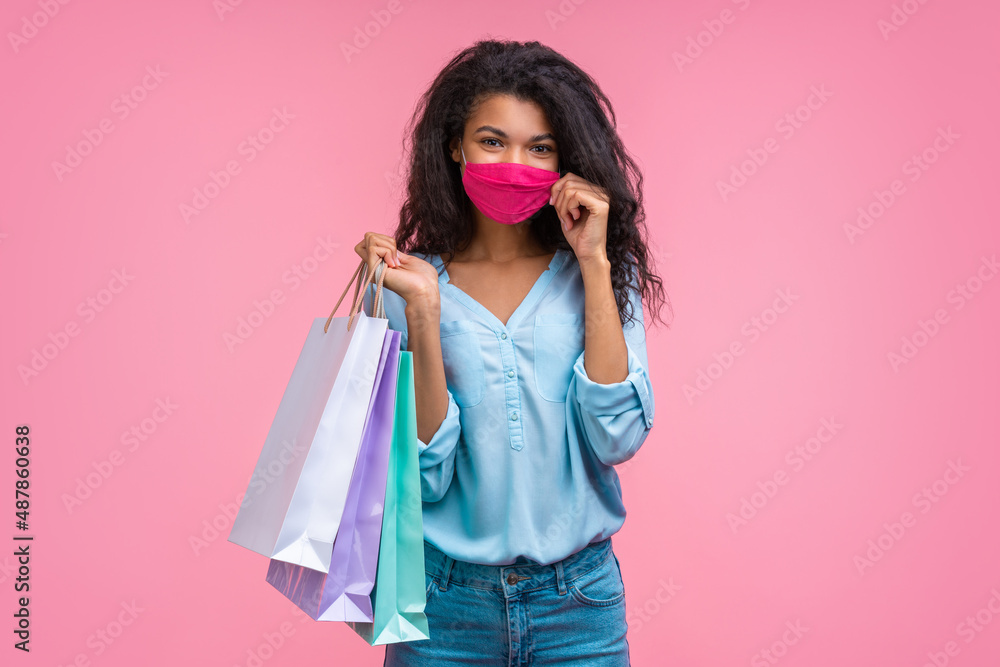 Portrait of beautiful stylish young woman in a medical protective mask on her face, holding shopping bags isolated over pink background Portrait of beautiful stylish young woman in a medical protective mask on her face, holding shopping bags isolated over pink background