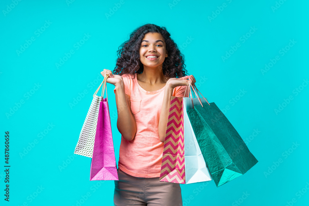 Studio shot of smiling beautiful young woman holding a bunch of shopping bags in her both hands, feeling happy about her purchases