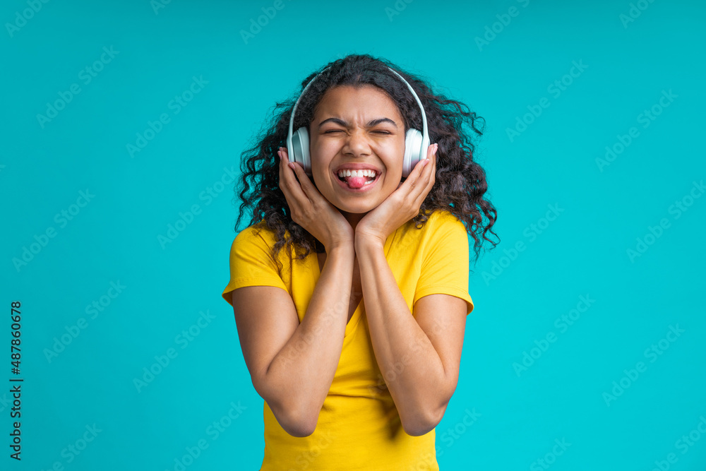 Studio portrait of cute and cheerful girl having fun listening to music with wireless headphones, isolated over bright colored blue background Studio portrait of cute and cheerful girl having fun listening to music with wireless headphones, isolated over bright colored blue background