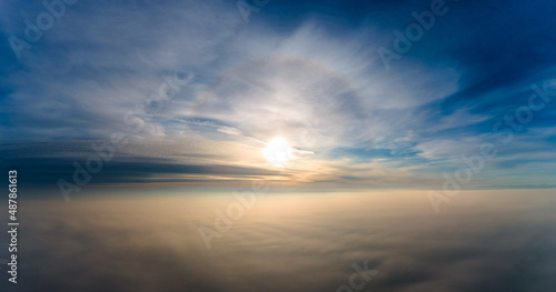 Aerial view of bright yellow sunset over white dense clouds with blue sky overhead