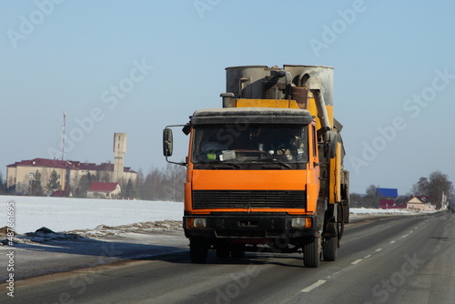 Yellow loaded small truck on suburban winter road in Europe. Front view closeup. Transportation logistics.
