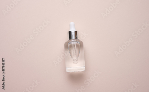 glass transparent white bottle with a pipette. Container for cosmetics, acids and oils on a beige background