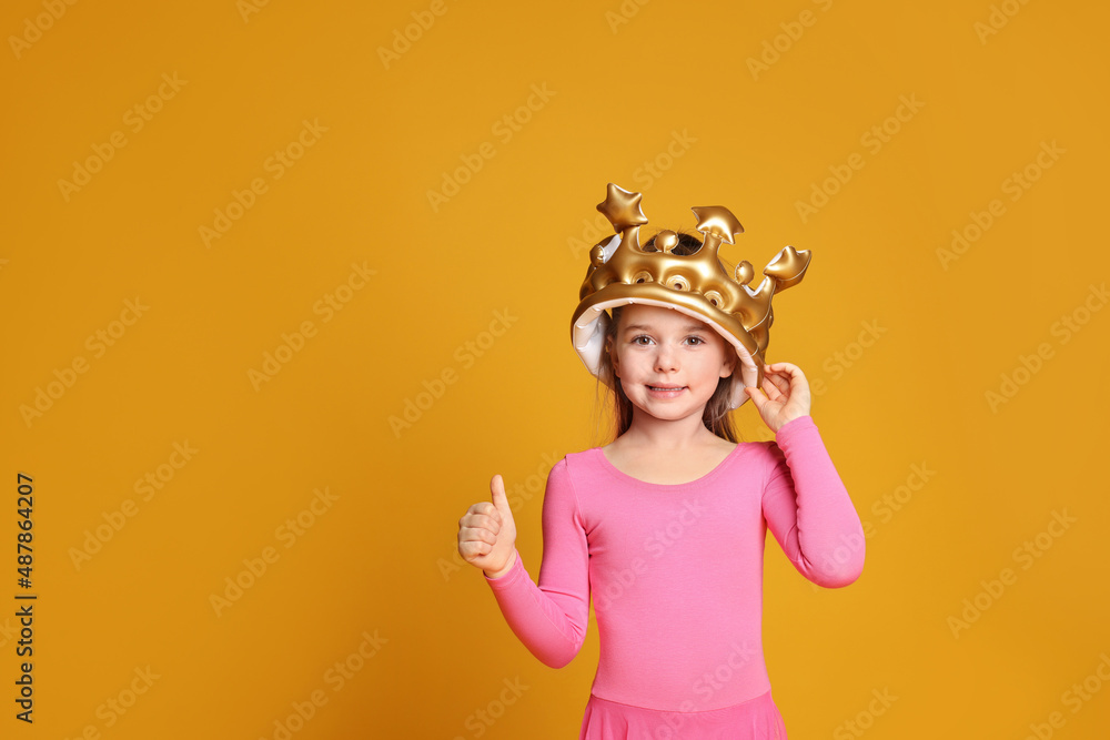 Cute girl in inflatable crown on yellow background, space for text. Little princess Cute girl in inflatable crown on yellow background, space for text. Little princess