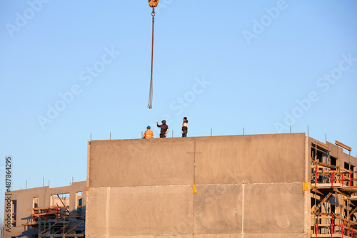 Pracownicy budowani podczas budowy domu na tle niebieskiego wieczornego nieba z dźwigiem budowlanym.