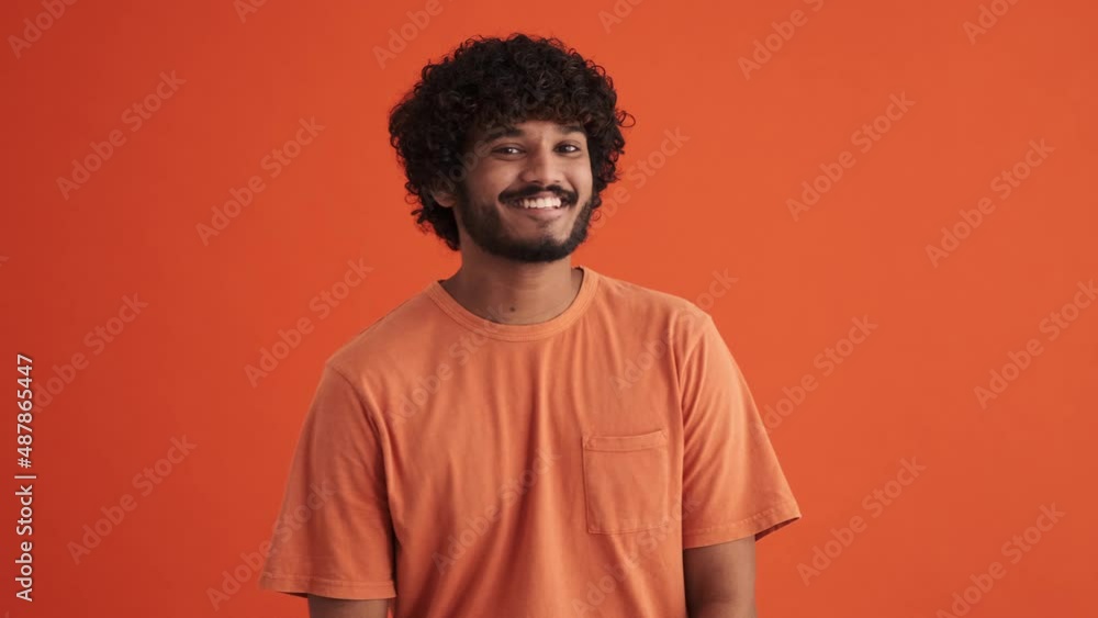 Smiling curly-haired Indian man winking at the camera in the orange studio Smiling curly-haired Indian man winking at the camera in the orange studio