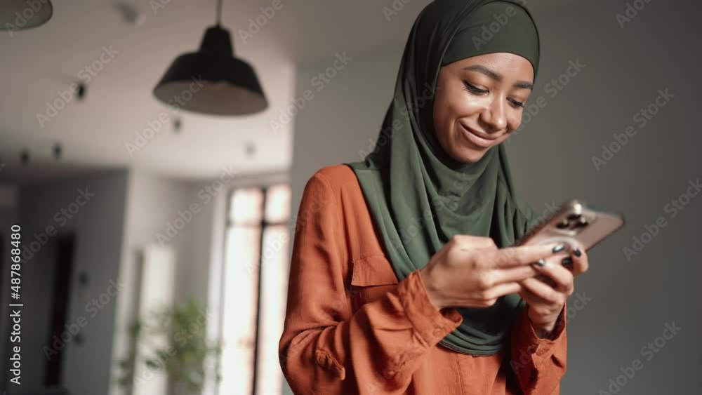 Smiling Muslim woman typing by phone at home Smiling Muslim woman typing by phone at home
