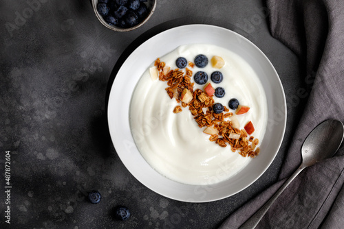 Blueberries in white yogurt with granola in white bowl on grey background. Top view. Breakfast idea. photo