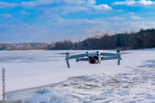 A drone hovering over the bank of a frozen river.