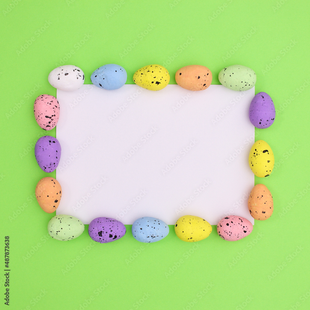 Easter copy space paper card note on bright green background with colorful vibrant eggs around. Flat lay minimal