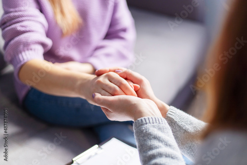 Close up of a female psychologist holding woman's hands during a therapy session. Psychotherapist supporting her depressed patient