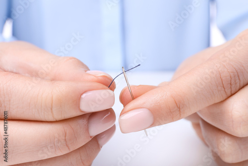 Woman threading sewing needle at table  closeup