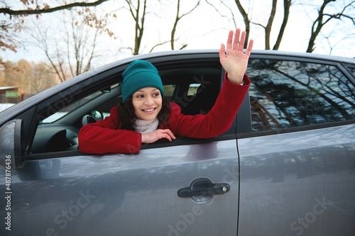 Happy female driver gesturing with hand, greeting someone, smiling with beautiful toothy smile photo