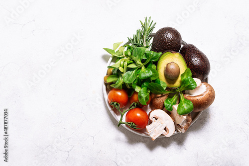 Fresh vegetables, fruit and mushrooms on the plate on white rustic background top view. Organic natural vegan food concept.