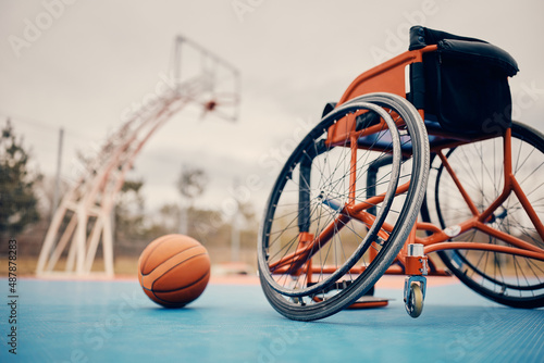 Sports wheelchair and basketball on outdoor sports court.