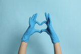 Doctor in medical gloves making heart with hands on light blue background, closeup