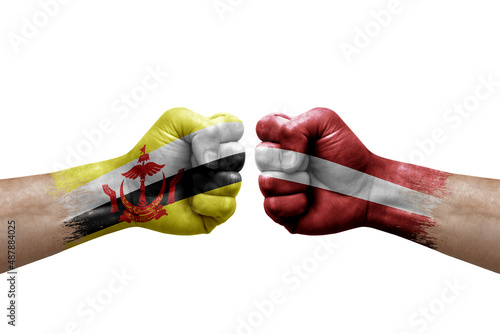 Two hands punch to each others on white background. Country flags painted fists, conflict crisis concept between brunei and latvia