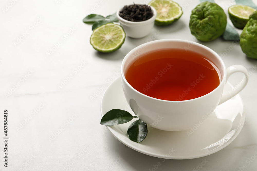Cup of tasty bergamot tea and fresh fruits on white table, space for text Cup of tasty bergamot tea and fresh fruits on white table, space for text