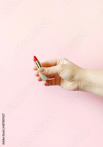 Red lipstick in a tube holds a female hand on a pink background. Cosmetic product for bright beauty creative makeup. Make-up artist tool.