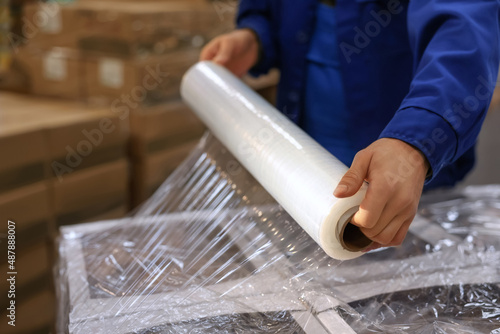 Fotografie Worker wrapping boxes in stretch film at warehouse, closeup