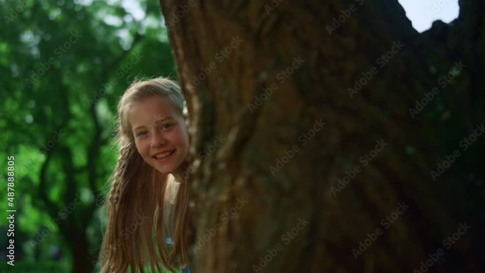 Little kid peeking tree trunk. Playful kid hide behind large plant on sunny day Little kid peeking tree trunk. Playful kid hide behind large plant on sunny day