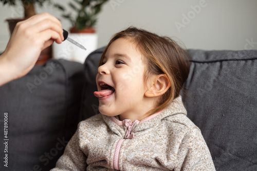 Foto Portrait of caucasian preschool girl taking vitamins with drops at home