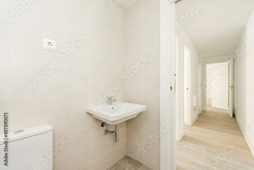 bathroom with white porcelain sink  hardwood floors in a long hallway with access to other rooms