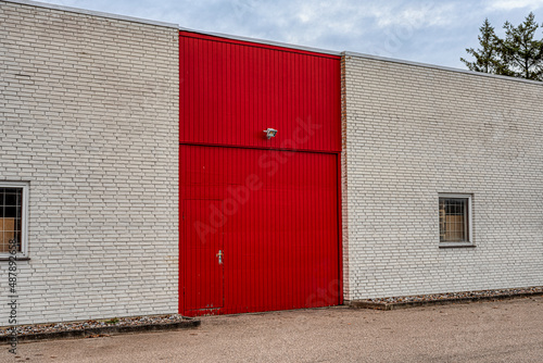 red door and gate on a white brick wall at the front of a storage with windows with grids © Stig Alenas
