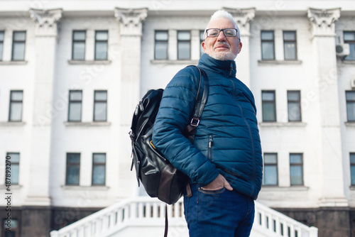 Active retirement concept. Portrait of handsome silver haired mature man watching signtseeing attractions in center of old European capital city. Nice winter day. Modern haircut, beard. Outdoor shot photo