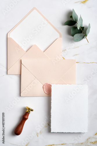 Elegant wedding stationery set. Wedding invitation card template, pastel pink envelopes, wax seal stamp, eucalyptus on marble table. Flat lay, top view