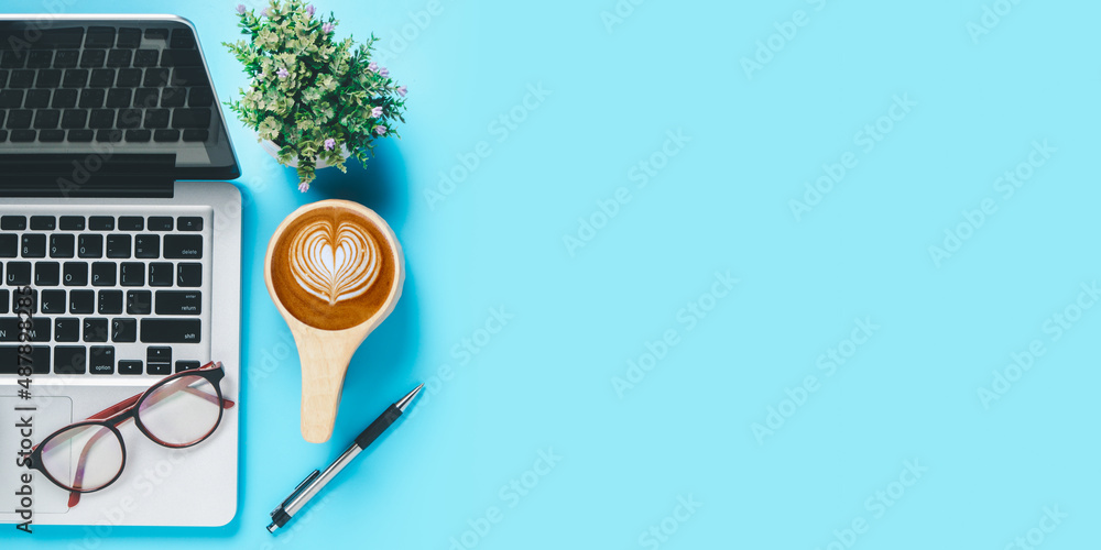 Office desk with computer, Pen, eyeglass, Cup of coffee on blue background, Top view with copy space, Mock up. Office desk with computer, Pen, eyeglass, Cup of coffee on blue background, Top view with copy space, Mock up.