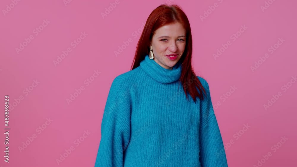 Smiling playful happy redhead teen girl in blue sweater blinking eye, looking at camera with toothy smile, winking and flirting, expressing optimism. Young pretty adult woman on pink studio background Smiling playful happy redhead teen girl in blue sweater blinking eye, looking at camera with toothy smile, winking and flirting, expressing optimism. Young pretty adult woman on pink studio background