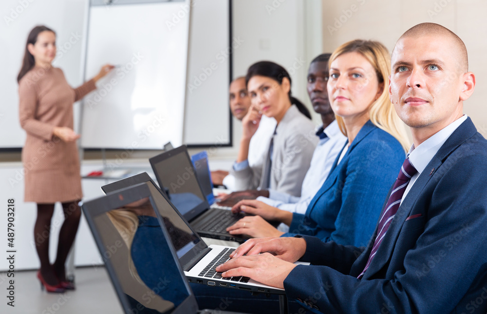 Obraz premium Side view portrait of multiethnic group of people sitting in row, working with laptops during business training. European man in focus of camera..