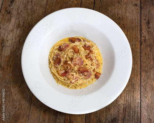 Pasta con salsa a base de huevo, tocineta y queso parmesano en un plato blanco sobre un fondo de madera