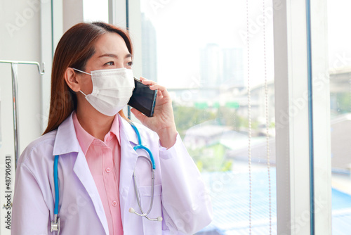 Beautiful Asian female doctor wearing a white mask Hold a smartphone and talk to the patient. Modern communication technology concept, patient care through smartphone. copy space
