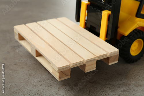 Toy forklift with wooden pallet on light grey table, closeup