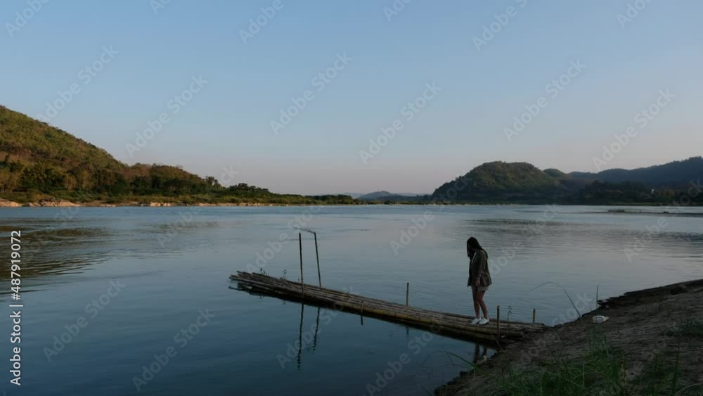 A young asian woman walking, sitting and playing with water on bamboo pier by the Mekong river A young asian woman walking, sitting and playing with water on bamboo pier by the Mekong river