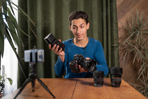 training for beginner photographers, online courses. A Muslim man records a video review of photographic equipment using an application on a smartphone. Radio synchronizers their purpose photo