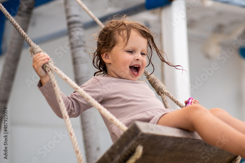 a little girl with curly hair swings on a swing and screams with happiness and joy.