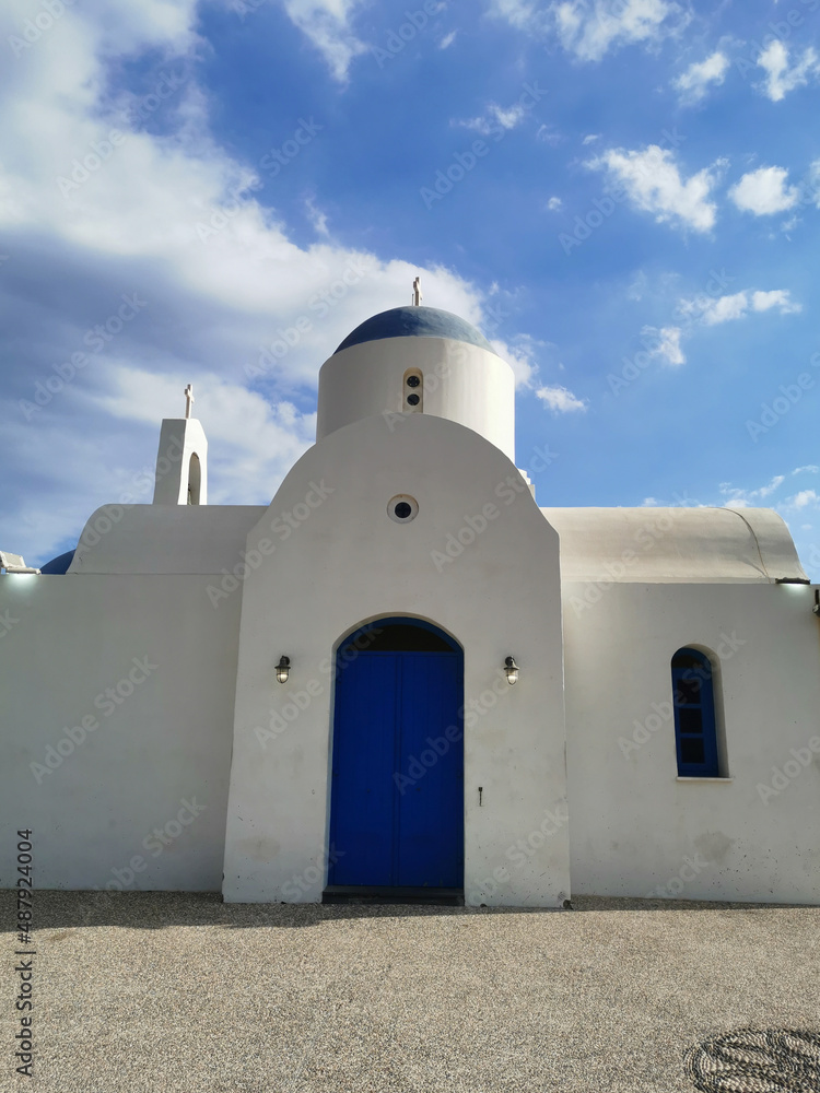 The Church of St. Nicholas the Wonderworker is white with a blue door against the backdrop of  the sky.