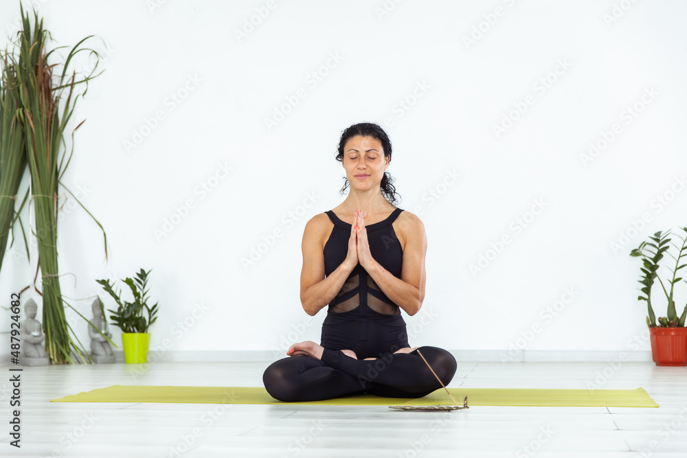 Young yogi woman meditates with smoking aroma stick while sitting on mat in yoga studio Young yogi woman meditates with smoking aroma stick while sitting on mat in yoga studio