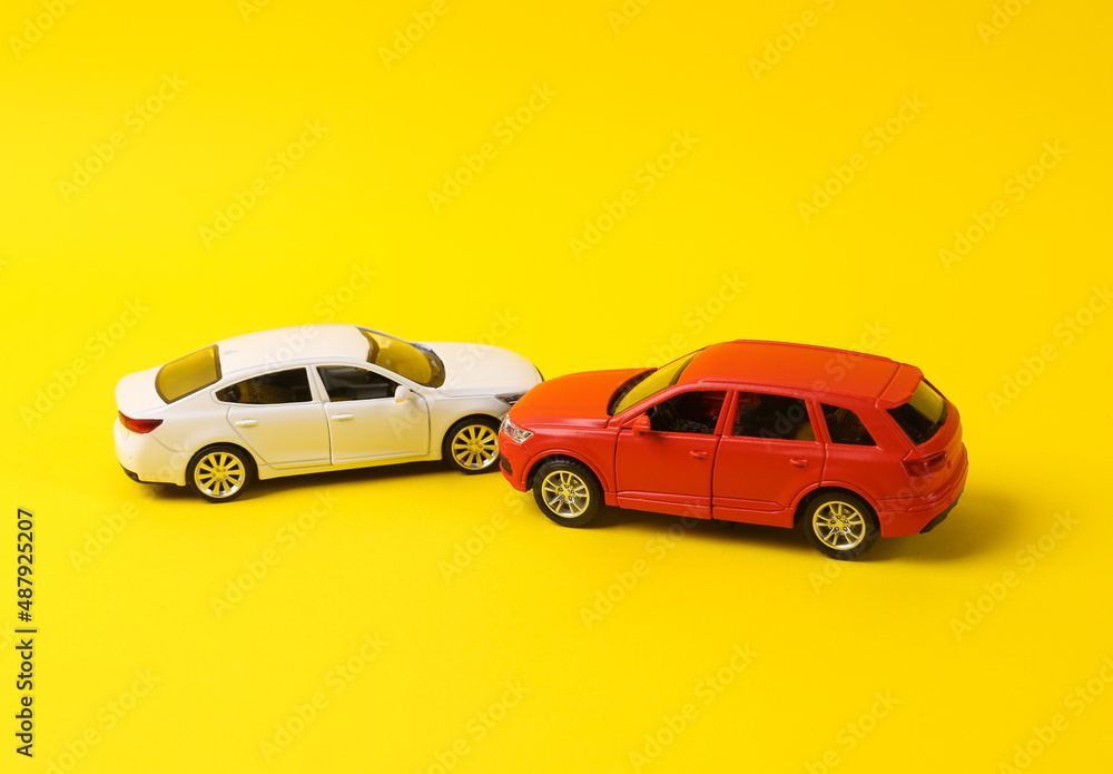 Two mini toy car crash on a yellow background, incident, car traffic accident