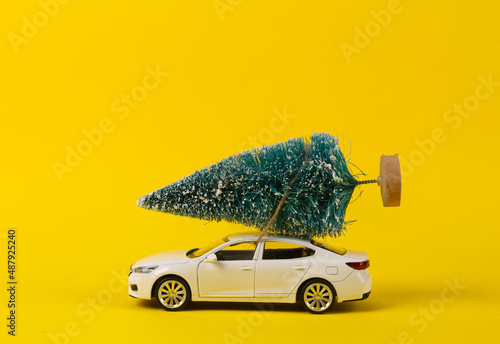 Toy car model with a Christmas tree on a yellow background. Happy Christmas concept, delivery