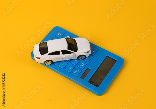 Toy car model with a calculator on a yellow background. Cost calculation, car purchase, fuel consumption, car service costs