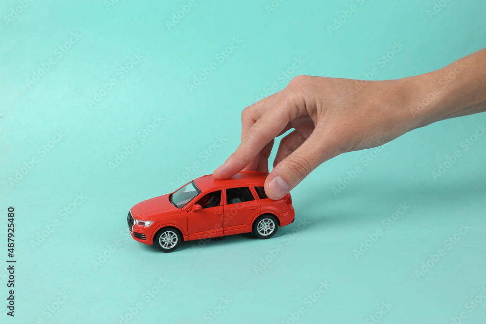 Woman's hand holding Toy car on blue background. Protection, insurance auto concept
